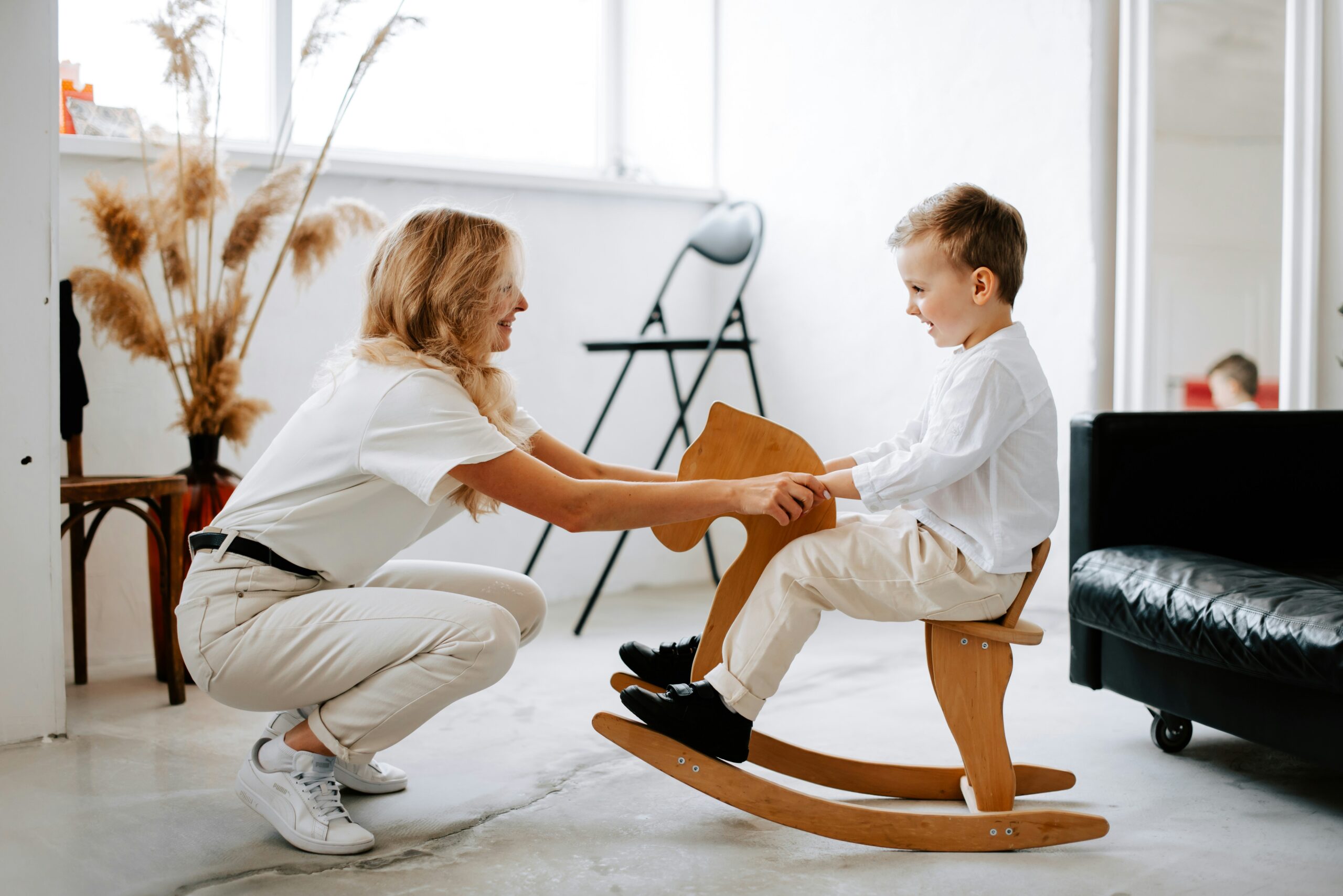 A female physical therapist providing pediatric rehabilitation to a young child on a wooden rocking horse in a modern clinic