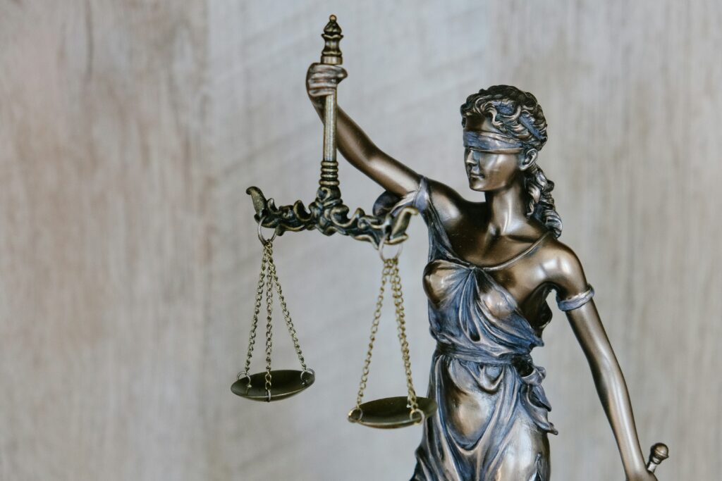 A bronze statue of Lady Justice, blindfolded and holding the scales of balance, against a neutral, light-textured background.