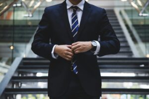A professional consultant in a navy blue suit and striped tie adjusting his cufflinks while standing on a modern glass staircase, representing the security provided by professional liability insurance.
