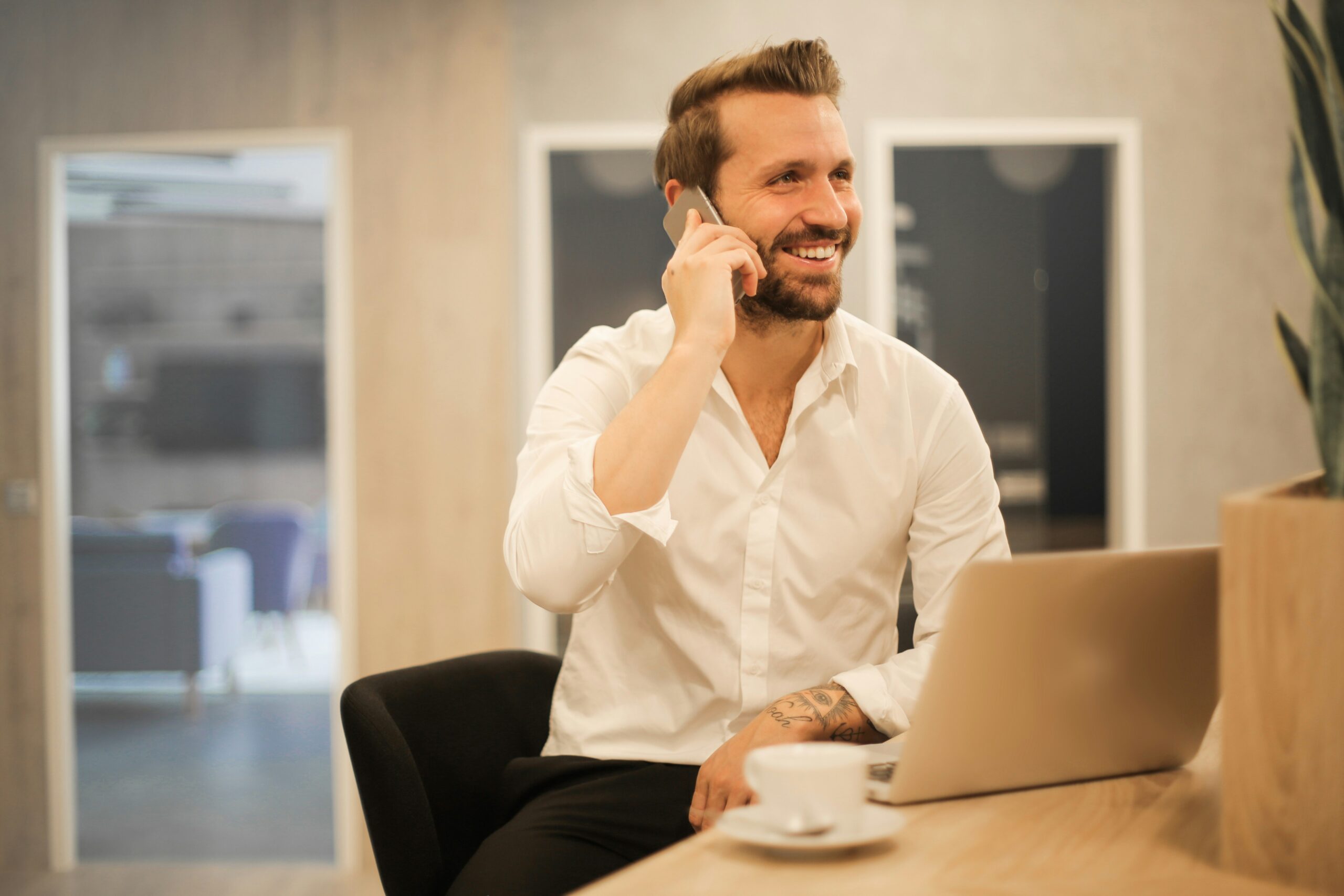 A smiling professional consultant in a modern office using a laptop and phone, representing the need for general liability and professional liability insurance for independent contractors.