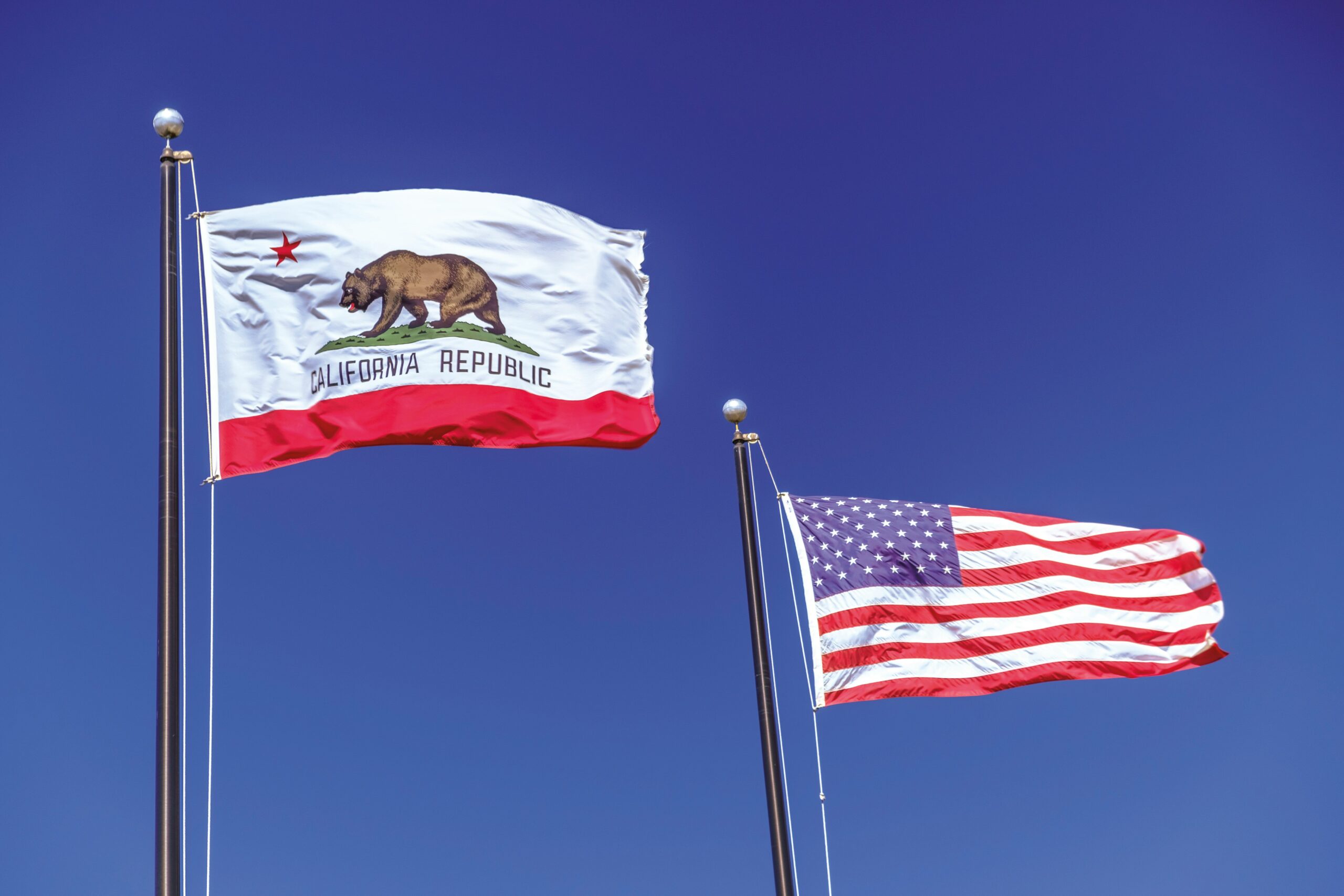The California state flag and American flag waving against a blue sky, representing the regulatory environment for professional liability insurance in California.