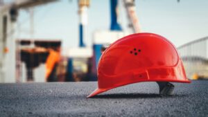 A bright red engineer's hard hat sitting on a concrete ledge at a construction site, representing safety and professional liability protection.