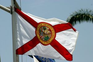 Florida state flag waving on a flagpole displaying the seal of the State of Florida against a clear sky.