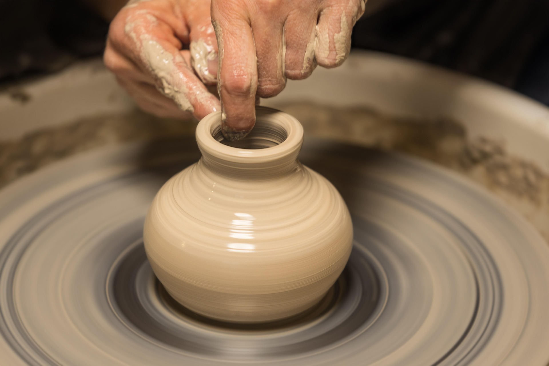Potter shaping a clay vase on a pottery wheel during the ceramic crafting process.