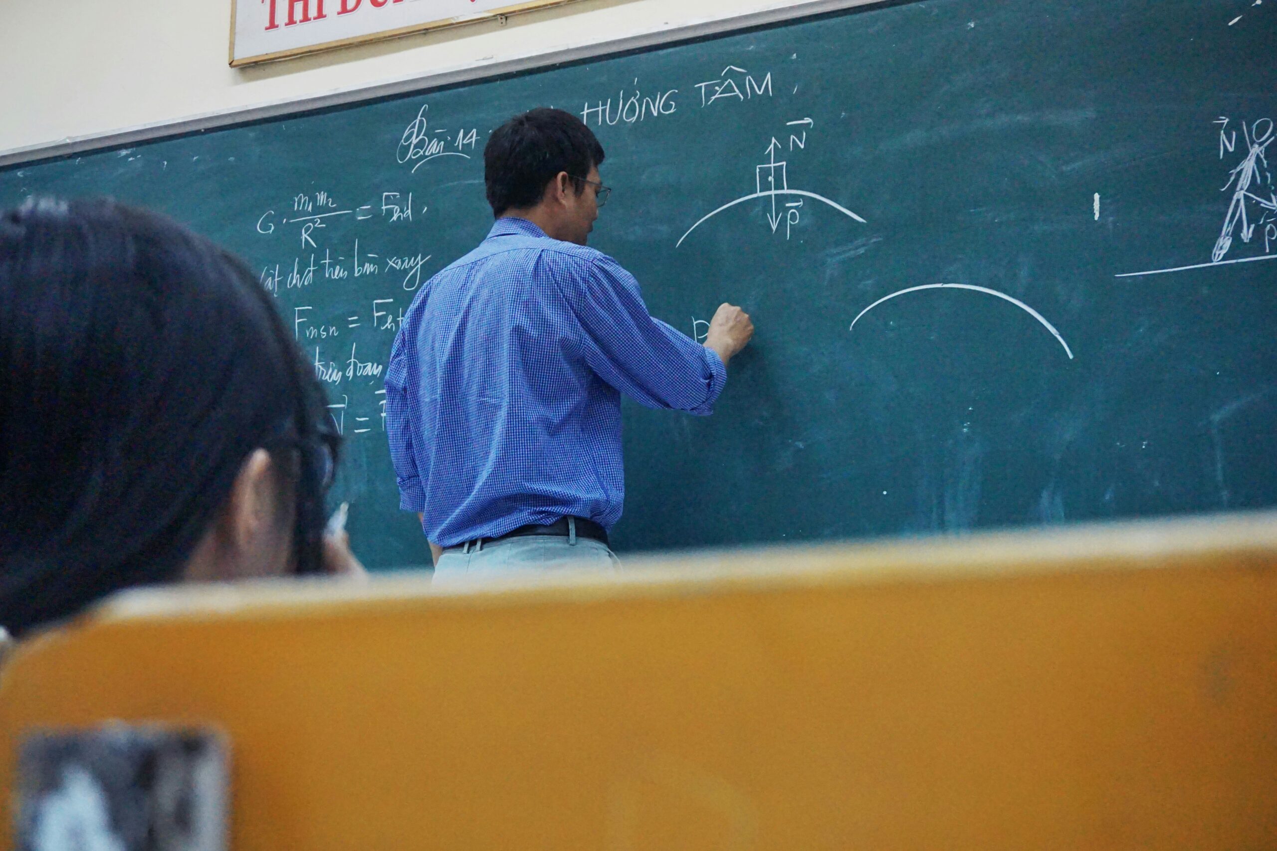 Physics teacher writing complex equations on a chalkboard during a classroom lecture, illustrating a consultant's duty of care and instruction.
