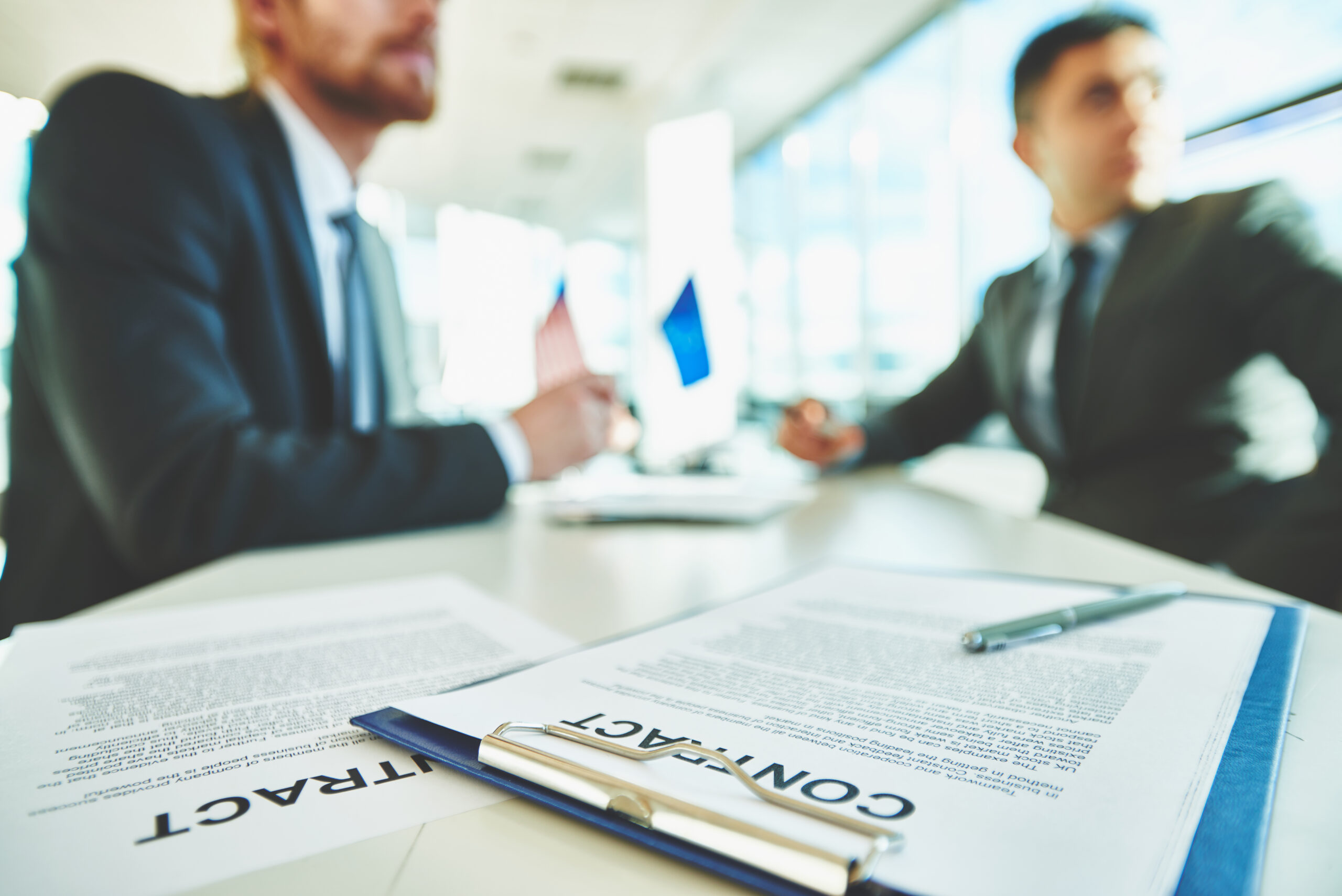 Two male consultants in suits discussing a professional liability contract in a bright, modern office.