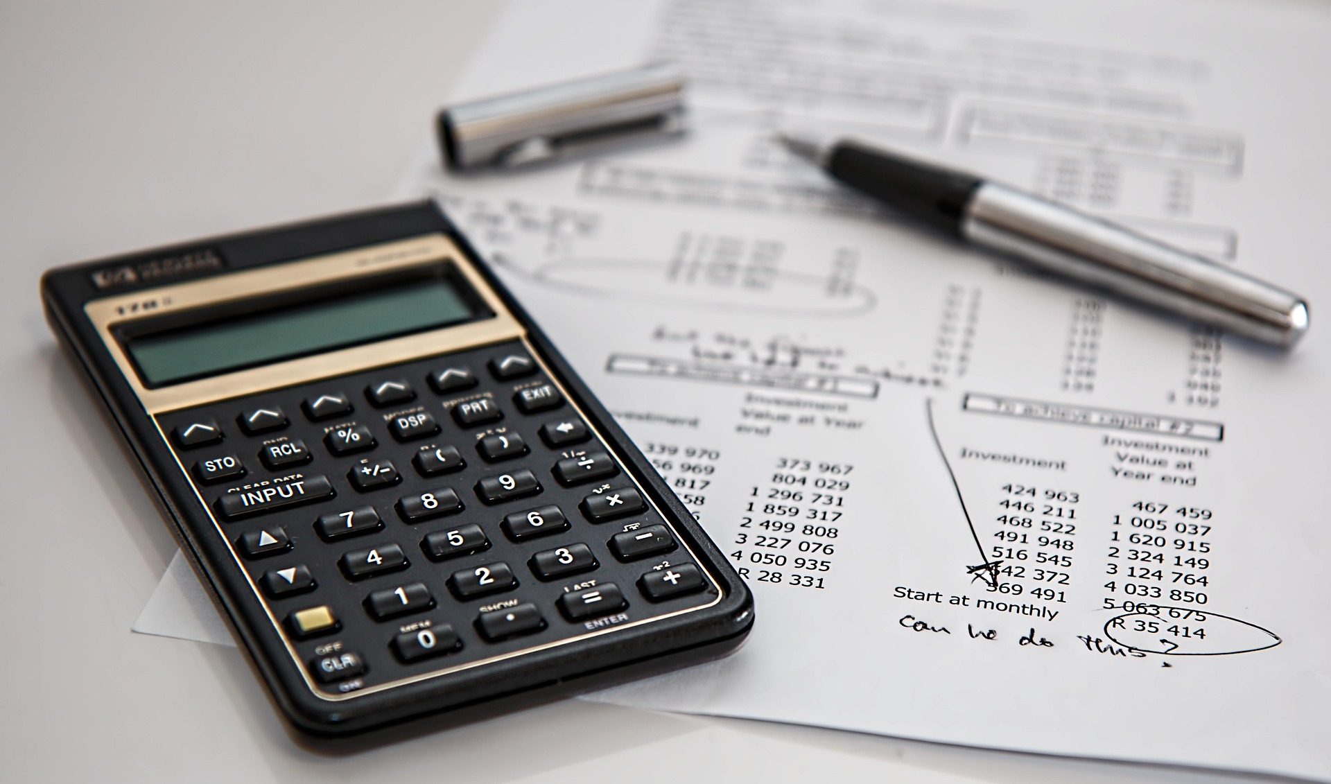 A financial calculator, pen, and investment documents on a desk, illustrating the cost analysis and risk management involved in choosing Errors and Omissions (E&O) insurance.